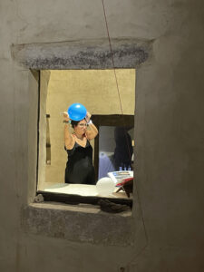 A lady holding a small, blue air balloon is visible through an opening in a wall.